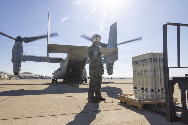 ローター回転中のMV-22Bオスプレイ（VMX-1所属）と、手前に積まれたソノブイの発射筒。米海兵隊MCASミラマーで2026年8月19日に実施されたロット受け入れ試験の様子。