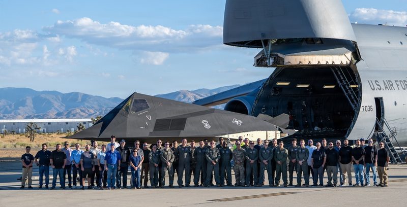 カリフォルニア州パームデールで、機首を開いたC-5M Super Galaxyの前に並ぶF-117A「The Overachiever」と関係者（2026年10月）